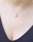 Necklace with a solitaire emerald pendant on a person wearing a dark blue top.