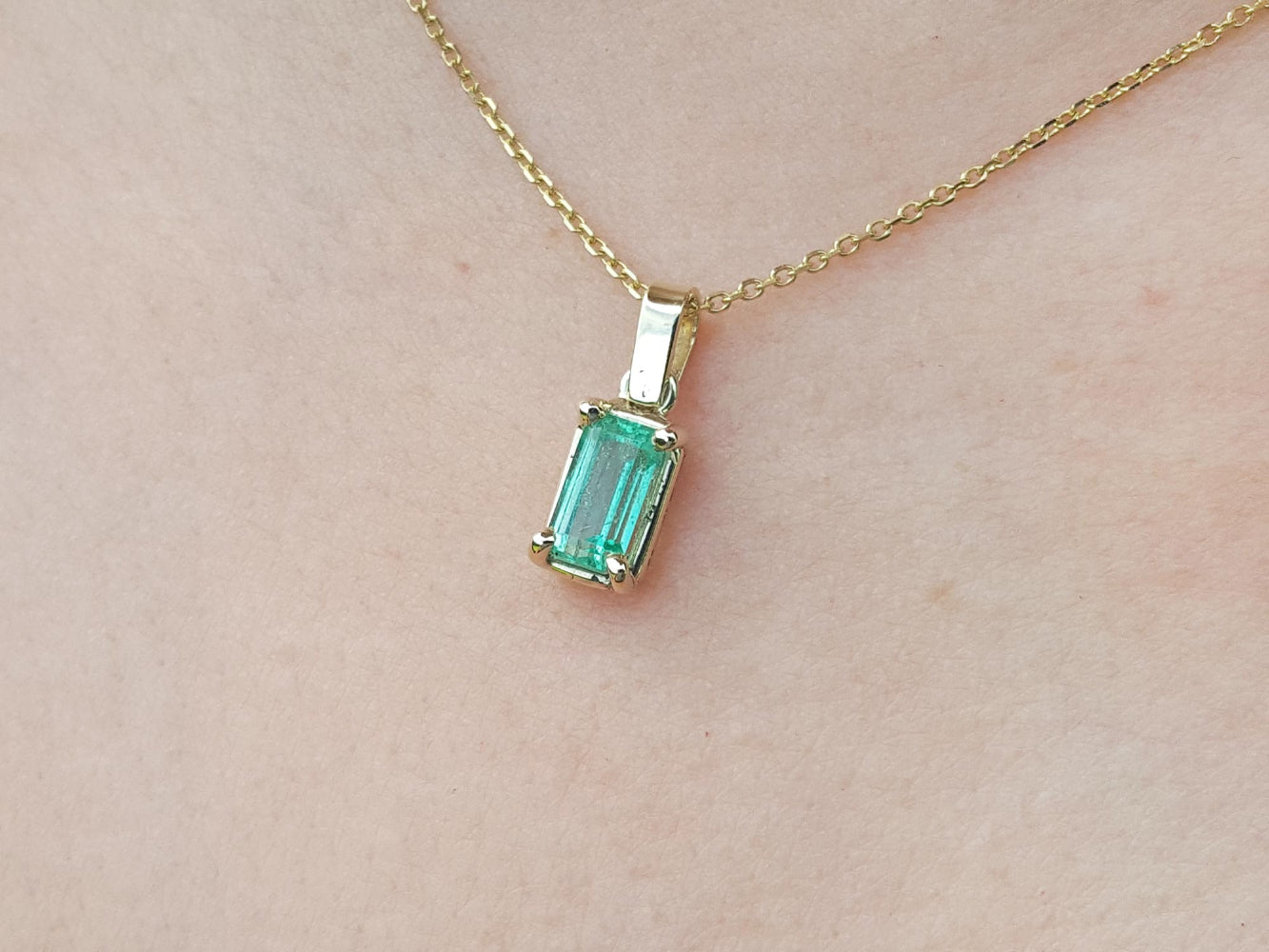 Gold necklace with a natural emerald pendant on a beige skin background