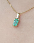 Gold necklace with a natural emerald pendant on a beige skin background