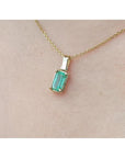 Gold necklace with a natural emerald pendant on a beige skin background