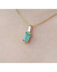 1.31 ct. emerald solitaire pendant in 14K yellow gold on a delicate chain, worn on a person.