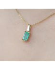 1.31 ct. emerald solitaire pendant in 14K yellow gold on a delicate chain, worn on a person.