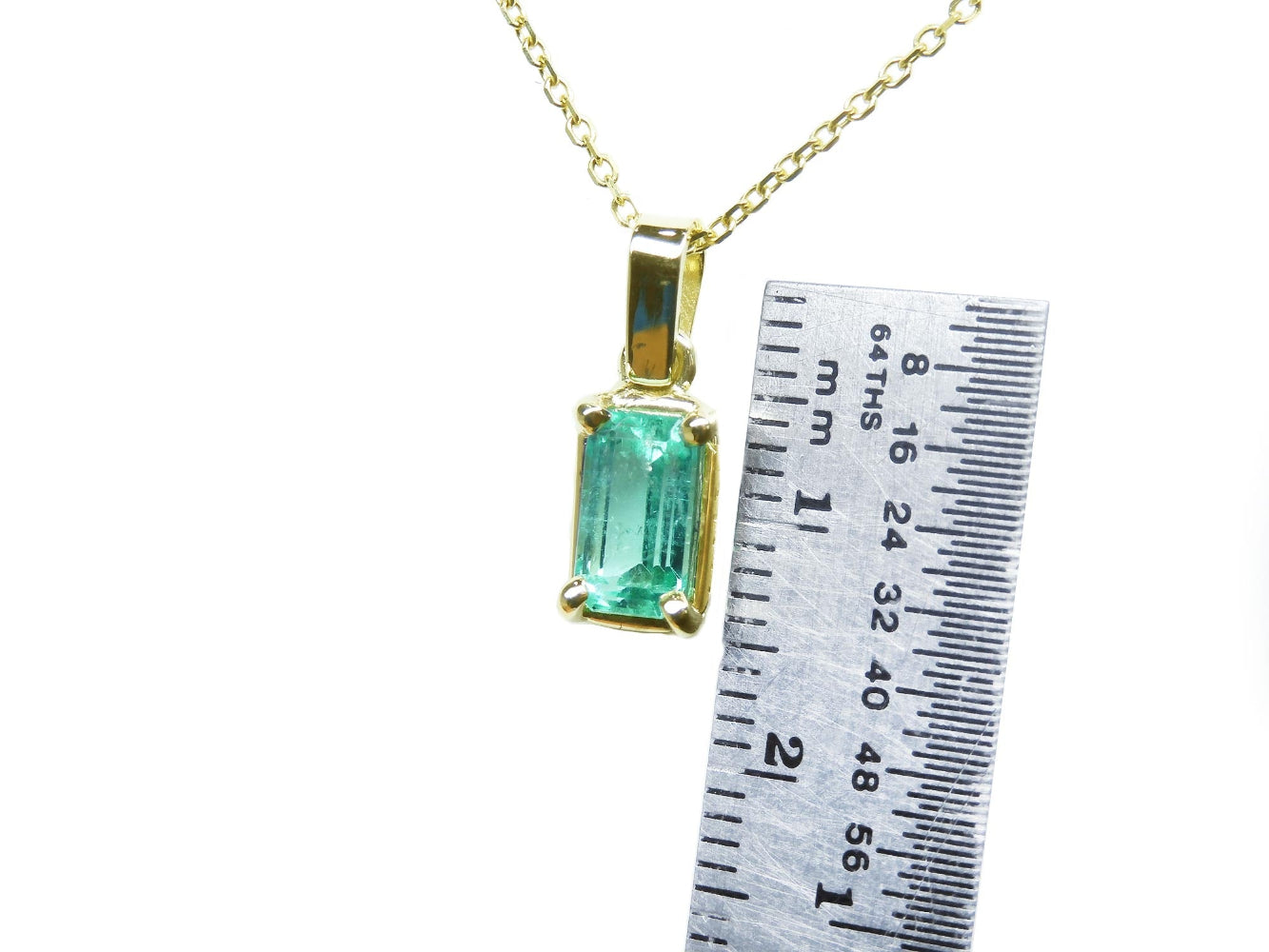 Gold pendant with a natural colombian emerald next to a ruler for scale on a white background