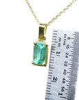 Gold pendant with a natural colombian emerald next to a ruler for scale on a white background