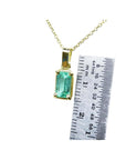 Gold pendant with a natural colombian emerald next to a ruler for scale on a white background