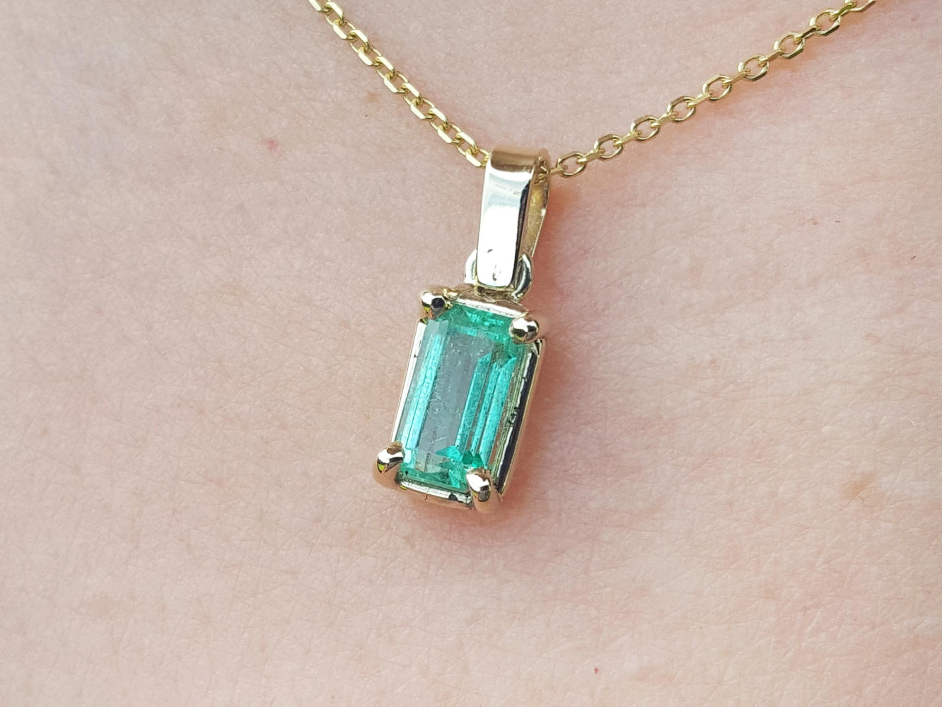 Gold necklace with a natural emerald pendant on a beige skin background