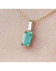 Gold necklace with a natural emerald pendant on a beige skin background