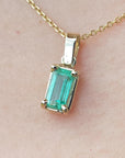 Gold necklace with a natural emerald pendant on a beige skin background