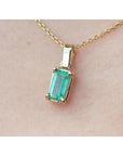 Gold necklace with a natural emerald pendant on a beige skin background