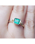 An emerald solitaire ring crafted in 14k yellow gold on a finger