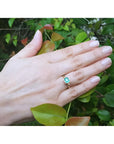 Hand wearing a 0.81 ct. medium bluish green emerald solitaire ring, bezel set in 14K yellow gold.