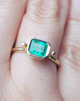 An emerald solitaire ring yellow gold on a finger