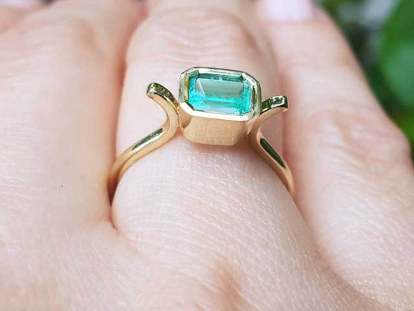 A solitaire emerald ring bezel set in yellow gold on a finger
