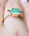 A solitaire emerald ring bezel set in yellow gold on a finger