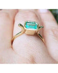0.81 ct. emerald solitaire ring, bezel set in 14K yellow gold, worn on a finger.