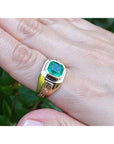 A 18k yellow gold ring with a bezel set genuine colombian emerald on a hand against a natural background.