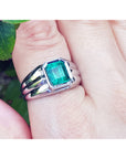 White gold ring for man with a square natural emerald on a finger against a natural background.