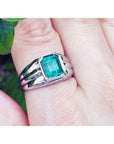 White gold ring for man with a square natural emerald on a finger against a natural background.