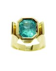 Emerald solitaire ring for women bezel set in 14k yellow gold.