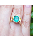 Emerald solitaire ring bezel set in 14k yellow gold on a hand.