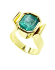 This emerald solitaire ring is on a tilted position, displaying the top bezel and side profile.