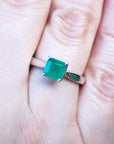 1.00 ct. square emerald cut Colombian emerald solitaire silver ring on a finger.