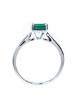 A lateral view of a solitaire sterling silver ring with a natural colombian emerald on a white background