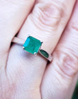 A genuine colombian emerald solitaire silver ring on a finger with a blurred background