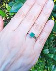 A close up of a hand wearing a genuine colombian emerald solitaire silver ring with a leafy background