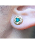 Close-up of a 14k yellow gold emerald stud earring on an ear.
