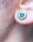 Close-up of a 14k gold emerald stud earring on a person's ear.