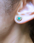 Close-up of a woman's ear wearing a gold stud emerald earring.