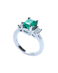 18K white gold three-stone emerald ring with a rectangular green emerald and two side emerald-cut diamonds.