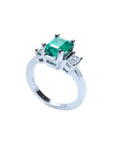 18K white gold three-stone emerald ring with a rectangular green emerald and two side emerald-cut diamonds.