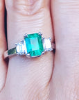 Women's emerald three stone ring side diamonds on a finger