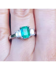 Women's emerald three stone ring side genuine emerald cut diamonds crafted in 18k white gold on a finger.