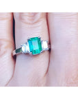 Women's emerald three stone ring side genuine emerald cut diamonds crafted in 18k white gold on a finger.
