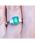 Women's emerald three stone ring side genuine emerald cut diamonds crafted in 18k white gold on a finger.