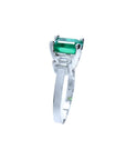 18K white gold three-stone ring with a rectangular emerald and two side emerald-cut diamonds.