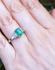 Emerald ring on a hand with a green leafy background