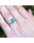 Three stone emerald ring with side diamonds on a hand, crafted in 18K white gold.