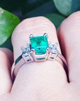 Brides' engagement emerald ring held between fingers against a natural background.