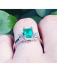 18K white gold three-stone emerald ring with a sparkling bluish-green center stone and side accent diamonds.