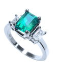 A tilted natural emerald and diamond three stone ring, top and side profile visibles.