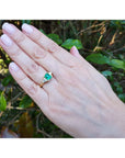 Hand wearing a three stone colombian emerald and trillion side diamond ring against a natural background.