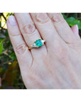 A woman's hand wearing a natural colombian emerald ring against a leafy background.