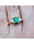 A colombian emerald and trillion side diamond ring in yellow gold on a hand