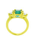 The lateral side view of a three stone colombian emerald ring for women with trillion diamonds in 18k gold.