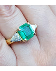 Women's emerald and trillion cut diamond ring on a hand.