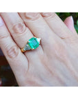 18k yellow gold ring with a large green emerald and two trillion side diamonds on a hand.